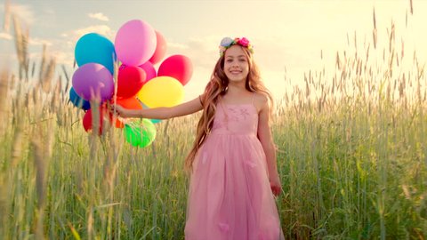 Young girl running through a wheat field with colour balloons during sunset