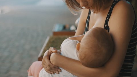 Woman is breastfeeding and rocking your little baby in the Park on a summer day. Close-up