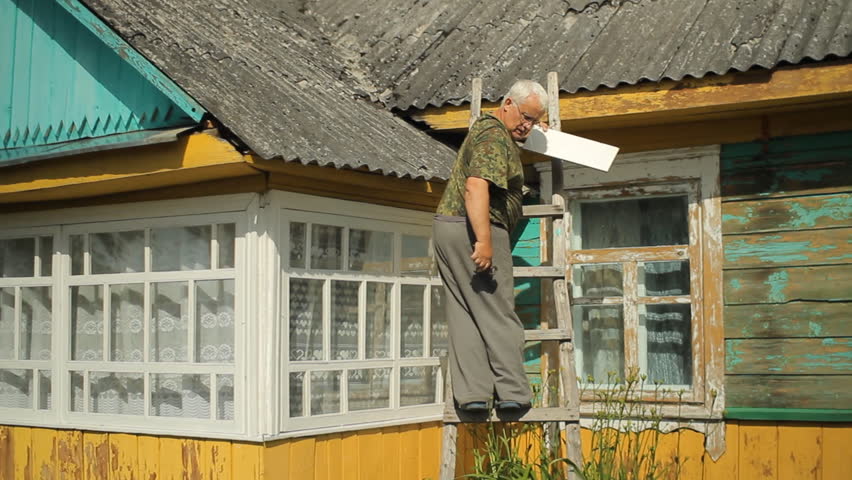 A man tries to fix the roof. He is standing on the stairs near the house