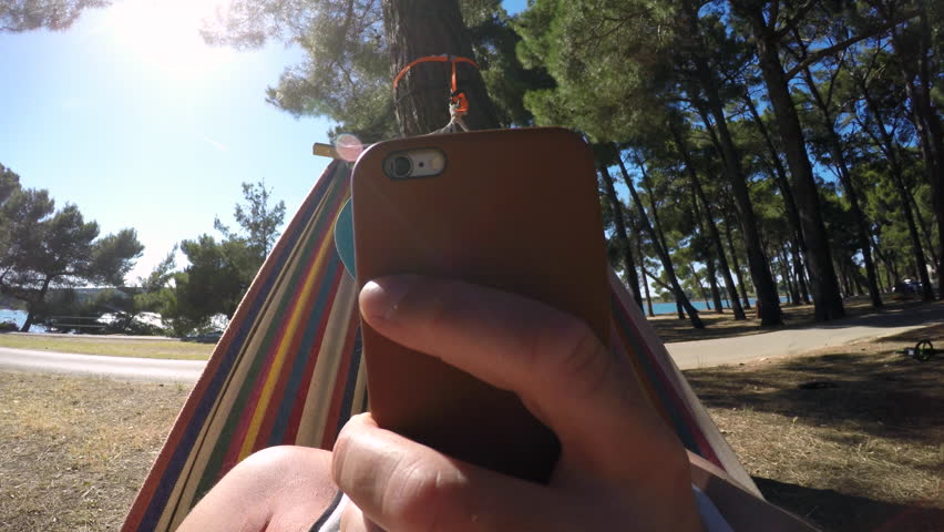 Man on smartphone in hammock on the beach