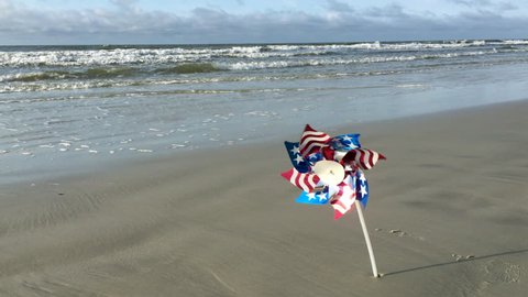 USA flag design pinwheel twirling in the wind on a sandy beach - Βίντεο στοκ
