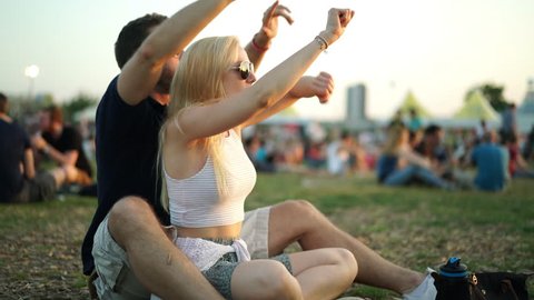 4k footage, happy young couple sitting on meadow at summer open air concert enjoying good music during late afternoon
