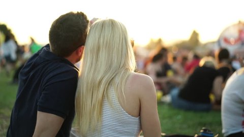 4k footage, couple sitting on festival meadow during summer sunset enjoying open air concert : vidéo de stock
