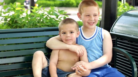 Boy tickling his brother on park bench