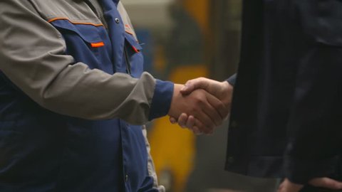 Two workers shake hands at the factory