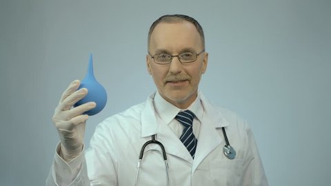 Funny doctor pressing on rectal syringe with smile on face, proctologist joking