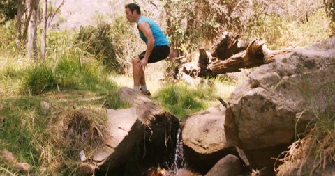 Hiker jumping across stream in forest