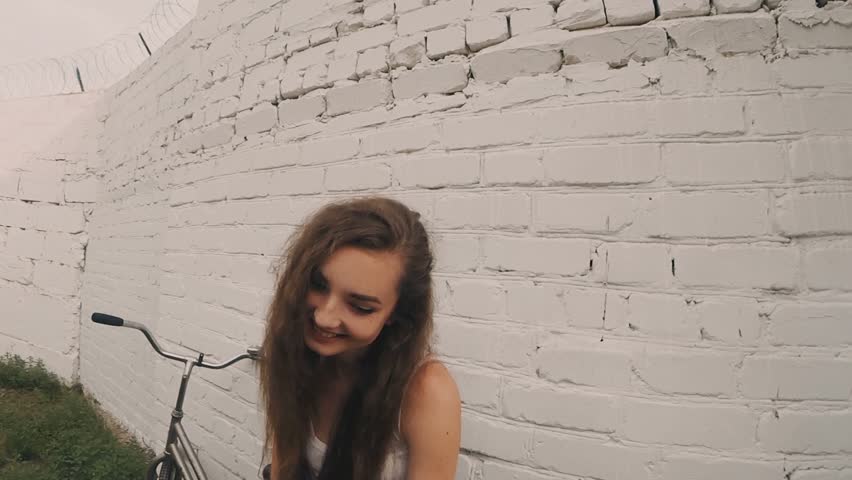 Happy girl near white wall, retro color shot. Young woman posing near bycicle leaning wall. Retro color.