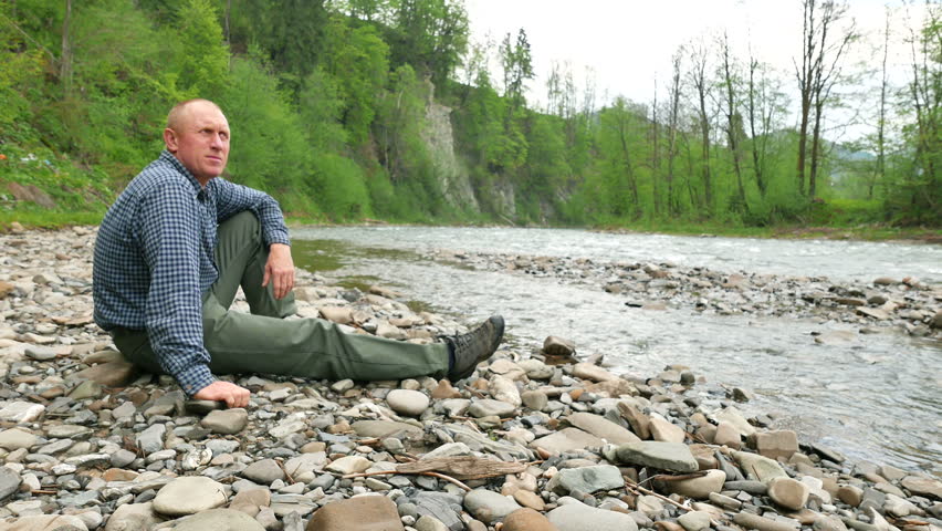 Rest of adult   man in trousers and  shirt near  river. 