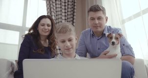 Happy family with cute dog talking to relatives using video chat on laptop at home 4K