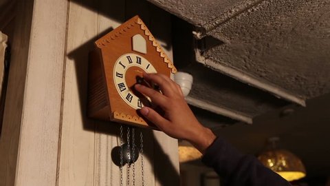 old cuckoo clocks hanging on  the camp in the room, a man takes  the clock from 1:00 to 2:00