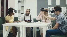 Three excited people trying virtual reality glasses and talking to bearded man with tablet at table on sofa - Powered by Shutterstock - Get 15% off with code: PIKWIZARD15