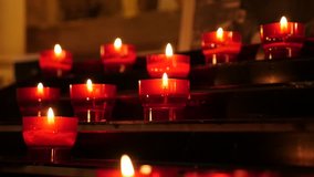 Fire tongues of catholic prayer red votive candles in  the rack 1080p HD footage - Lot of wax votive cups arranged in Christian church slow tilt slow-mo HD video