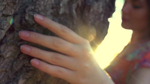 Beautiful young woman enjoying nature, touching tree outdoor. Beauty model girl walking in summer park. Person Hand Touches Tree closeup. Environmental protection concept. Slow motion, full HD 1080p