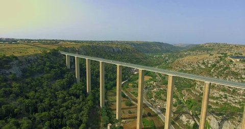 Top view of modern tall bridge spanning above green valley, with car traffic moving across .