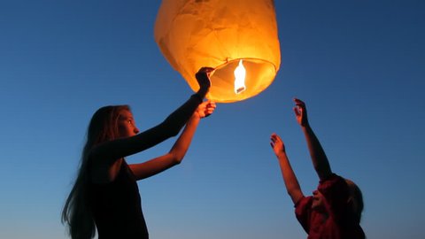 Two young girls launching a Chinese sky fly fire lantern to make a wish, summer holidays, celebration, family, children
