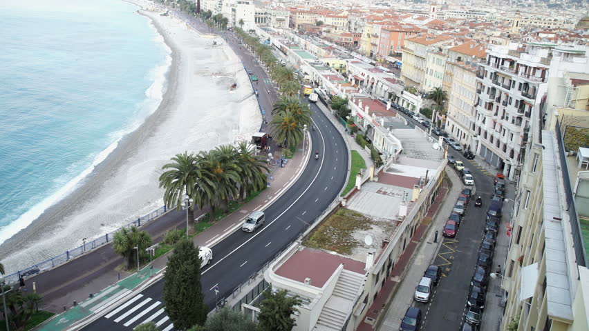 Along the promenade walk tourist and people who live in france. By seaside riding motorbikes on the road. On the seashore buildings historic architecture. Nice in spring season. French riviera
