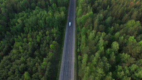 Aerial view flying over old patched two lane forest road with cars van moving green trees of dense woods growing both sides - shot with drone quad copter birds eye view perspective from above 