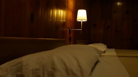 A lamp shines in a wood paneled motel room.