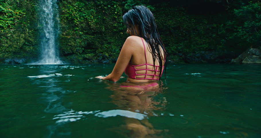 Young woman swimming under jungle waterfall