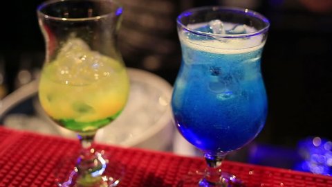 Barman preparing two colorful exotic cocktails in night club