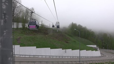 Gondola lift line move above curved mountain road, foggy weather, look back from moving cabin. MDG transportation system, dull scene, early spring at mountainous area