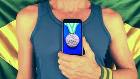 Brazilian athlete with Brazil colored wristbands scrolling through bronze, and silver medals on his smartphone, ending on gold with a thumbs up