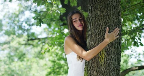 On a sunny day a woman embracing the tree as a sign of love for nature. Nature that she loves and protects because the tree is a symbol of life. The naturalist woman is carefree and smiling