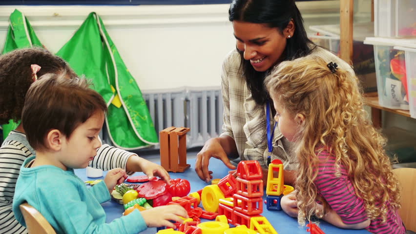 Teacher playing with building blocks and other toys at a classroom table with her nursery students.  Royalty-Free Stock Footage #17913613