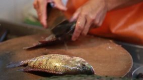 Local fish vendor scales and cleans a tilapia