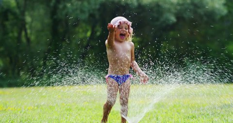 
a sweet little girl playing with garden sprinkler .
the girl gets wet completely it's very hot and happy day . concept nature and happy kids water in slow motion, pure water concept. happiness baby