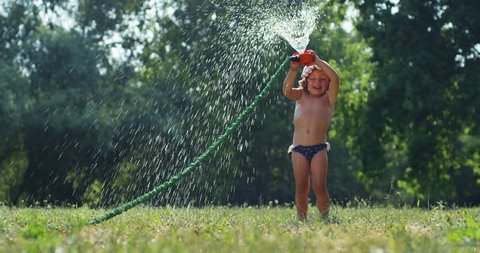 
a sweet little girl playing with garden sprinkler .
the girl gets wet completely it's very hot and happy day . concept nature and happy kids water in slow motion, pure water concept. happiness baby