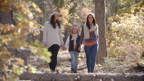 Female parents walk in a forest holding hands with daughter
