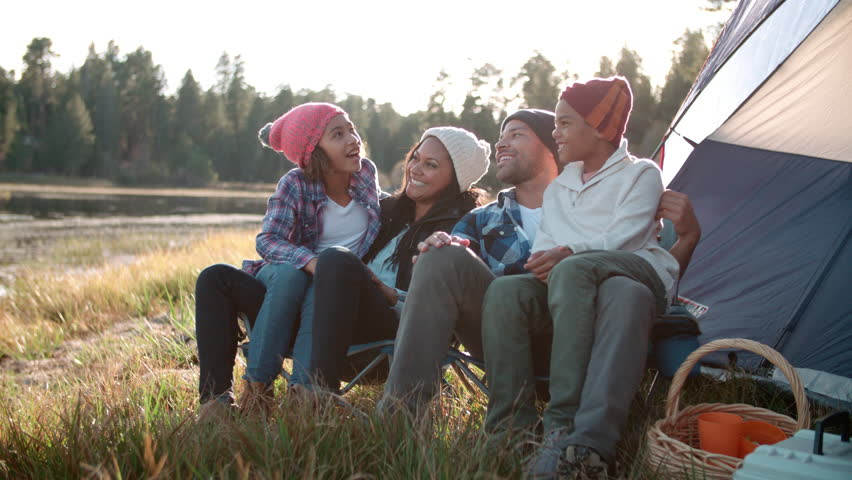 Parents and two children relaxing outside tent on camping trip