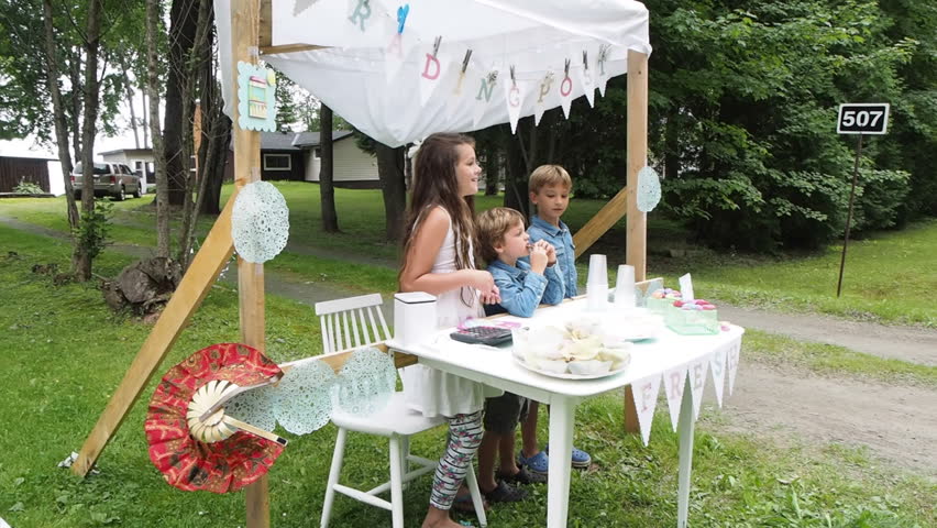 Children running roadside lemonade stand in summer on the side of the road trying to earn money. Little entrepreneurs setting up business to make money on side of road.