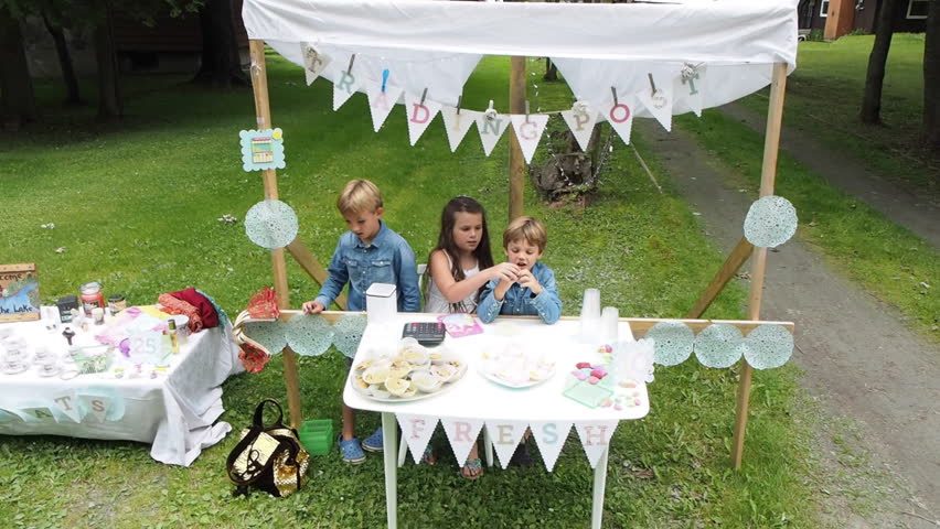 Children running roadside lemonade stand in summer on the side of the road trying to earn money. Little entrepreneurs setting up business to make money on side of road.