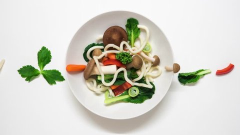 Vegetables and udon noodles becoming a soup. Fresh ingredients entering the plate and than they are cooked. Stop motion animation on white background. 4K resolution