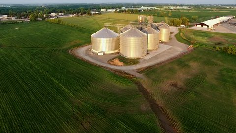 Aerial view of modern stainless steel agricultural grain silos at sunrise.
