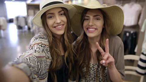 Twin teenage girls smiling in swimsuits posing for camera selfie while shopping in clothing retail store.
