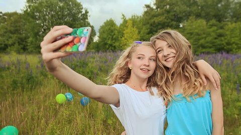Two young blonde girls are photographed on the phone. Make selfie.