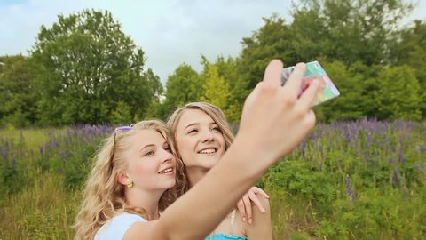 Two beautiful young girls taking self portrait outdoors on green spring park background