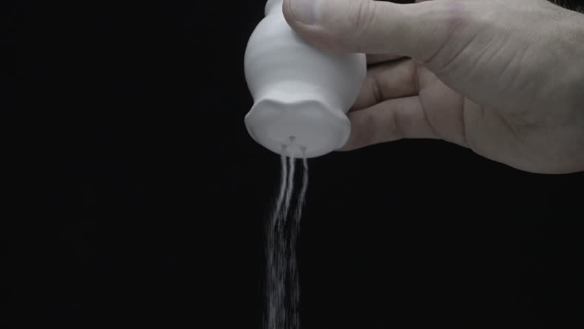 Hand shakes the salt cellar and salted food on a black background. Salt flies straight into the camera on white background. Bottom view. Slow motion, high speed camera, 250fps