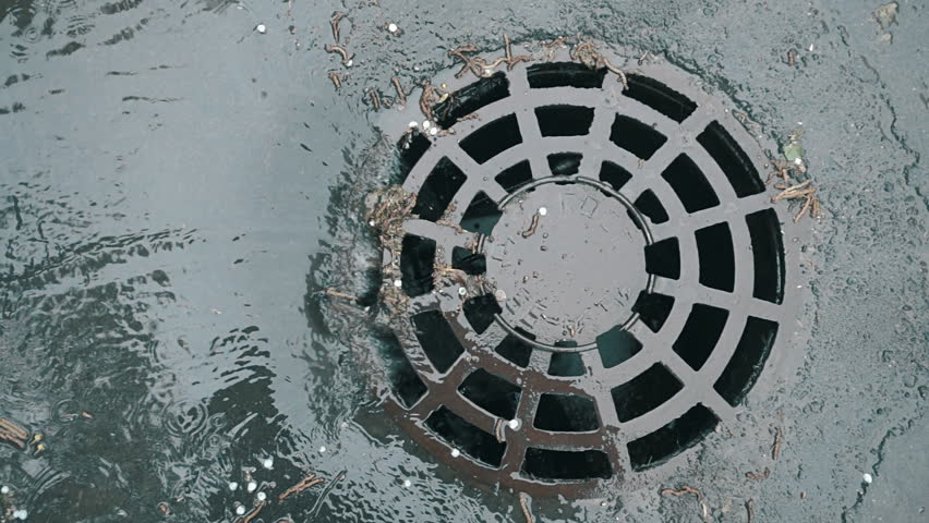 Rainwater flows on the road and fall into the metal hatch with holes drain. Slow motion, high speed camera, 250fps