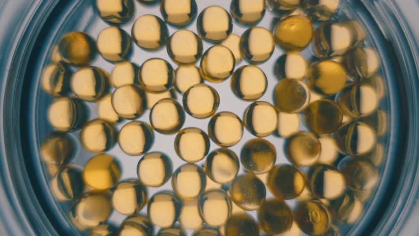 Transparent yellow medical capsules in a glass bowl is refracting light. Closeup