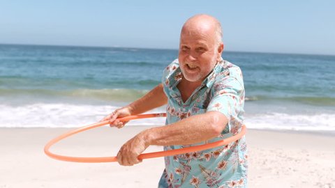 an elderly man doing hula hoop on the beach