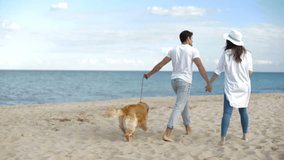 Romantic young couple walking on the sea shore with dog and holding hands