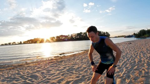 Strong male runner at the beach takes a break to get his breath back, slow-motion