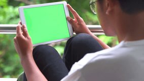 Man Sits on chair Using Tablet PC Smart Phone Mobile Device in Nature with Green Screen and enjoy listening to music video. 