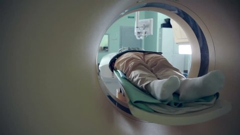 Unrecognizable hospital patient lying on MRI, tomograph, scanner, moving to and from the camera. Slider shoot.
