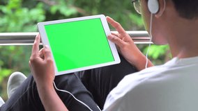 























































Man Sits on chair Using Tablet PC Smart Phone Mobile Device in Nature with Green Screen and enjoy listening to music video.